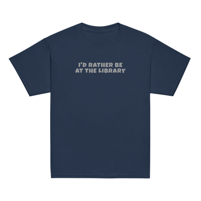 "I’d rather be at the library" printed on a navy youth classic tee laying on a flat surface