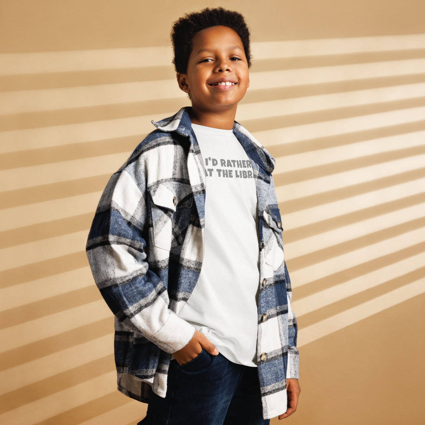 "I’d rather be at the library" printed on a white youth classic tee worn by a male also wearing a jacket
