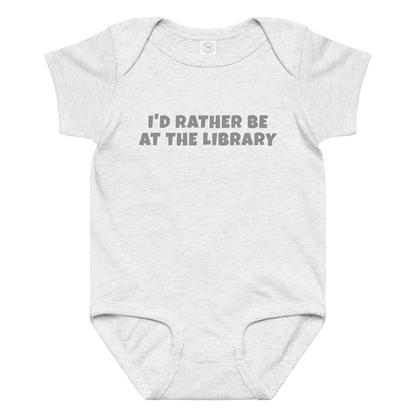 "I’d rather be at the library" printed on a ash baby jersey bodysuit laying on a flat surface amongst other clothes
