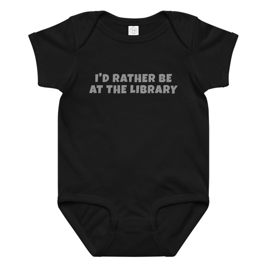"I’d rather be at the library" printed on a black baby jersey bodysuit laying on a flat surface amongst other clothes