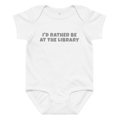 "I’d rather be at the library" printed on a white baby jersey bodysuit laying on a flat surface amongst other clothes