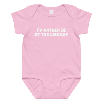 "I’d rather be at the library" printed on a pink baby jersey bodysuit laying on a flat surface amongst other clothes