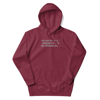 "I'd rather be unemployed in greenland" printed on a maroon unisex hoodie laying on a flat surface with the hood up