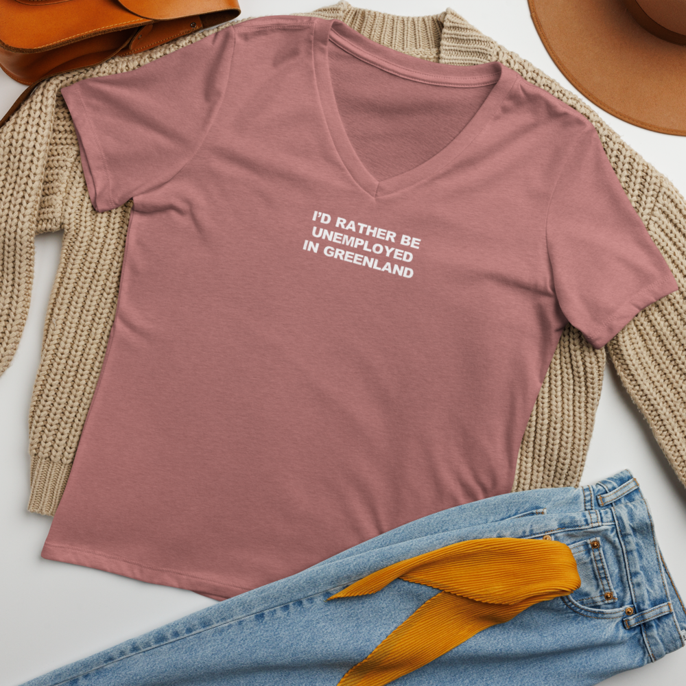 "I'd rather be unemployed in greenland" printed on a heather mauve women's relaxed v-neck t-shirt laying on a flat surface amongst other clothes