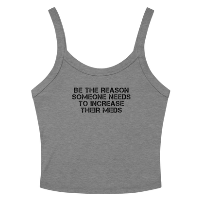 "Be the reason someone needs to increase their meds" printed on a athletic heather women's micro-rib tanktop laying on a flat surface amongst sunglasses and shorts