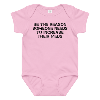 "Be the reason someone needs to increase their meds" printed on a pink baby jersey bodysuit laying on a flat surface amongst other clothes