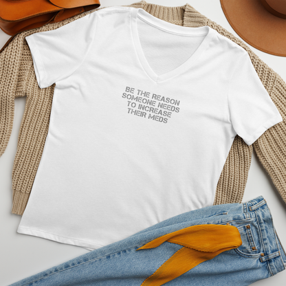 "Be the reason someone needs to increase their meds" printed on a solid white blend women's relaxed v-neck t-shirt laying on a flat surface amongst other clothes