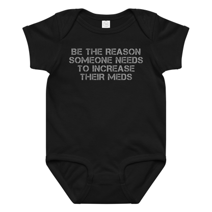 "Be the reason someone needs to increase their meds" printed on a black baby jersey bodysuit laying on a flat surface amongst other clothes