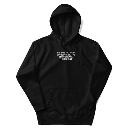 "Be the reason someone needs to increase their meds" printed on a black unisex hoodie laying on a flat surface with the hood up