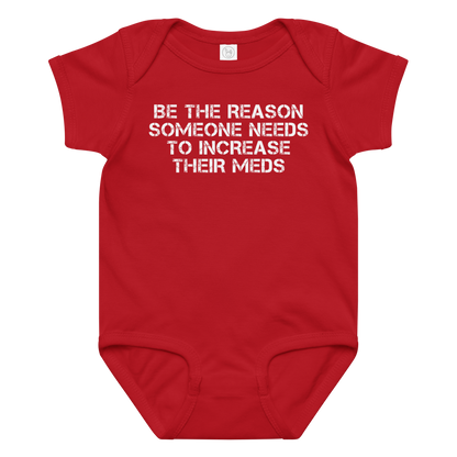 "Be the reason someone needs to increase their meds" printed on a red baby jersey bodysuit laying on a flat surface amongst other clothes