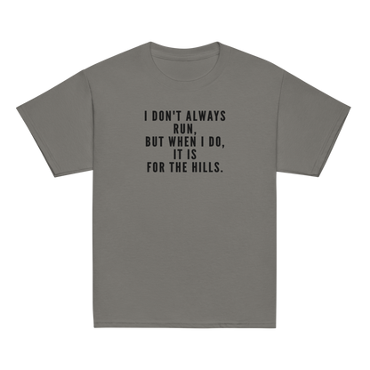 "I don't always run, but when I do, it is for the hills." printed on a charcoal youth classic tee laying on a flat surface