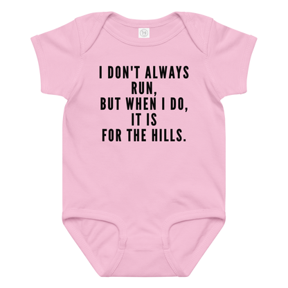 "I don't always run, but when I do, it is for the hills." printed on a pink baby jersey bodysuit laying on a flat surface amongst other clothes