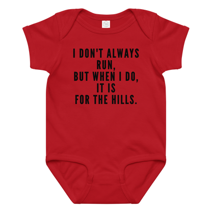 "I don't always run, but when I do, it is for the hills." printed on a red baby jersey bodysuit laying on a flat surface amongst other clothes