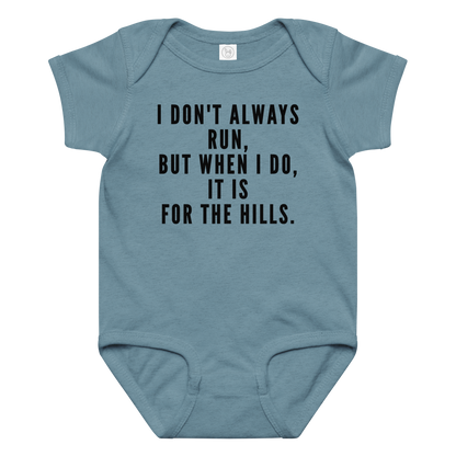 "I don't always run, but when I do, it is for the hills." printed on a vintage indigo baby jersey bodysuit laying on a flat surface amongst other clothes