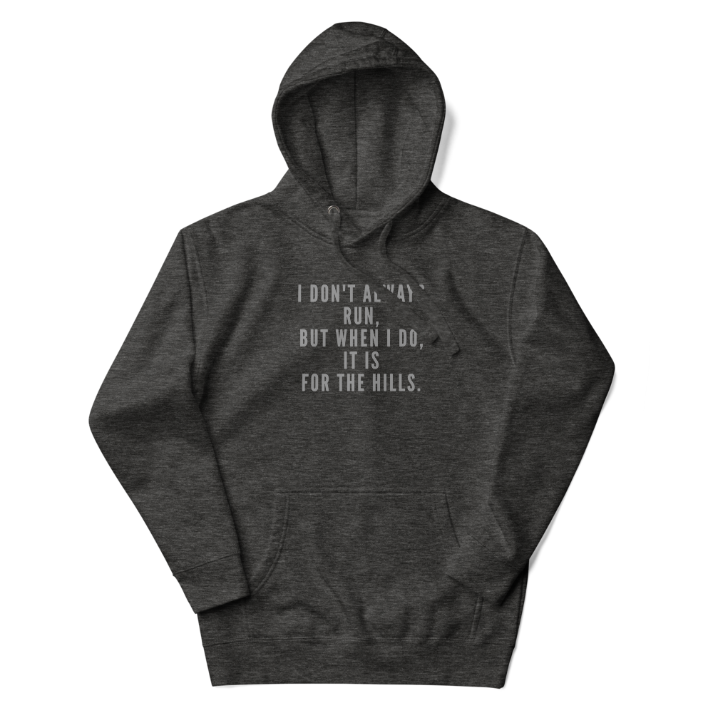 "I don't always run, but when I do, it is for the hills." printed on a charcoal heather unisex hoodie laying on a flat surface with the hood up