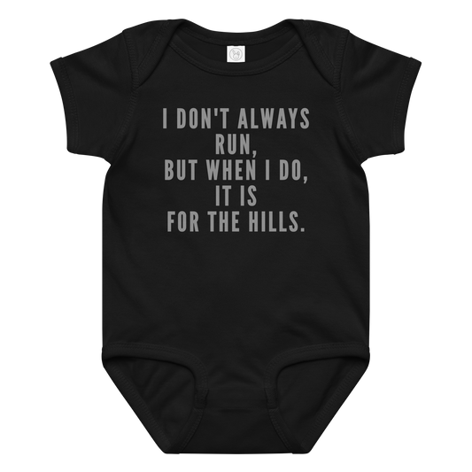"I don't always run, but when I do, it is for the hills." printed on a black baby jersey bodysuit laying on a flat surface amongst other clothes