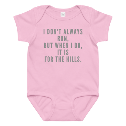 "I don't always run, but when I do, it is for the hills." printed on a pink baby jersey bodysuit laying on a flat surface amongst other clothes