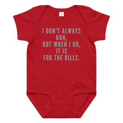 "I don't always run, but when I do, it is for the hills." printed on a red baby jersey bodysuit laying on a flat surface amongst other clothes