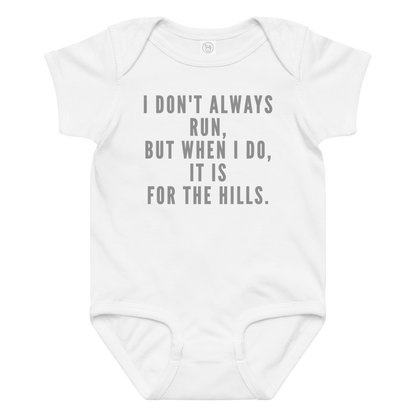 "I don't always run, but when I do, it is for the hills." printed on a white baby jersey bodysuit laying on a flat surface amongst other clothes