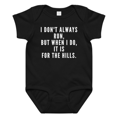 "I don't always run, but when I do, it is for the hills." printed on a black baby jersey bodysuit laying on a flat surface amongst other clothes