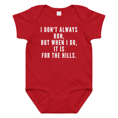 "I don't always run, but when I do, it is for the hills." printed on a red baby jersey bodysuit laying on a flat surface amongst other clothes