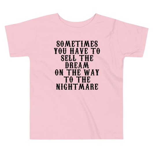 "Sometimes you have to sell the dream on the way to the nightmare" printed on a pink toddler short sleeve tee laying on a flat surface