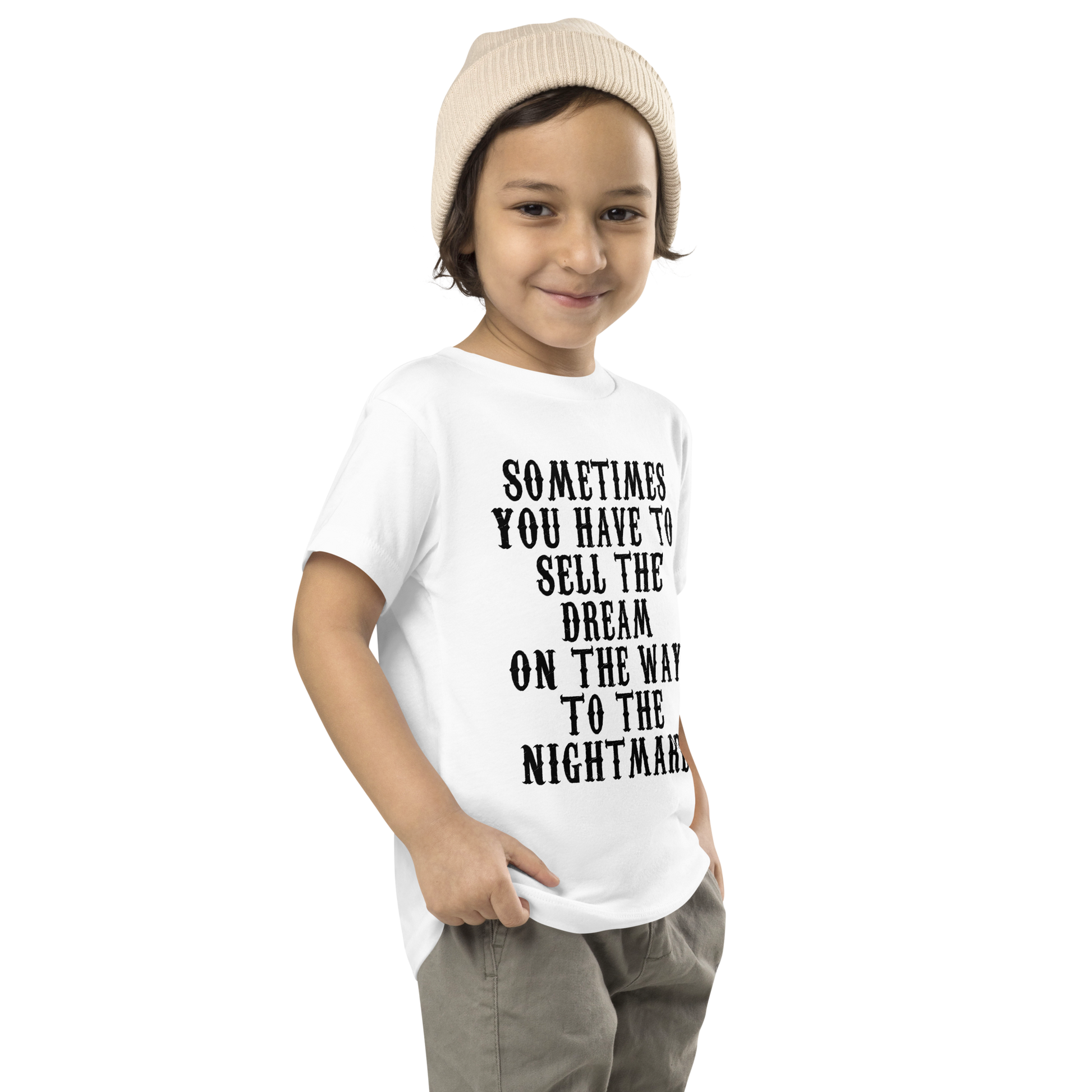 "Sometimes you have to sell the dream on the way to the nightmare" printed on a white toddler short sleeve tee worn by a male who is also wearing a knit cap