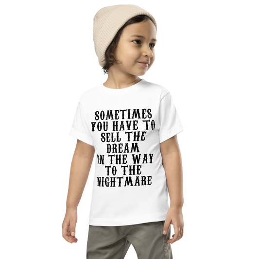"Sometimes you have to sell the dream on the way to the nightmare" printed on a white toddler short sleeve tee worn by a male wearing a cap