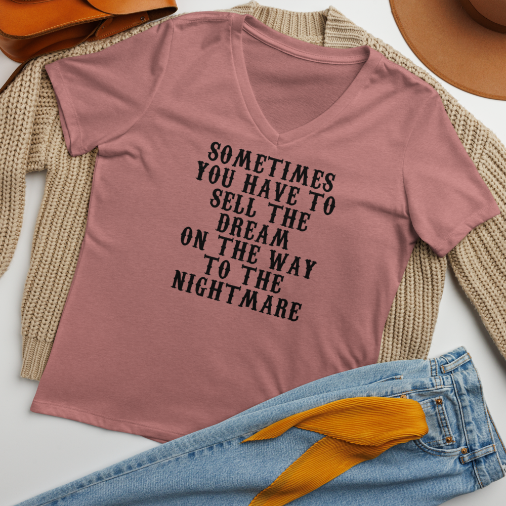 "Sometimes you have to sell the dream on the way to the nightmare" printed on a heather mauve women's relaxed v-neck t-shirt laying on a flat surface amongst other clothes