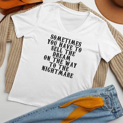"Sometimes you have to sell the dream on the way to the nightmare" printed on a solid white blend women's relaxed v-neck t-shirt laying on a flat surface amongst other clothes