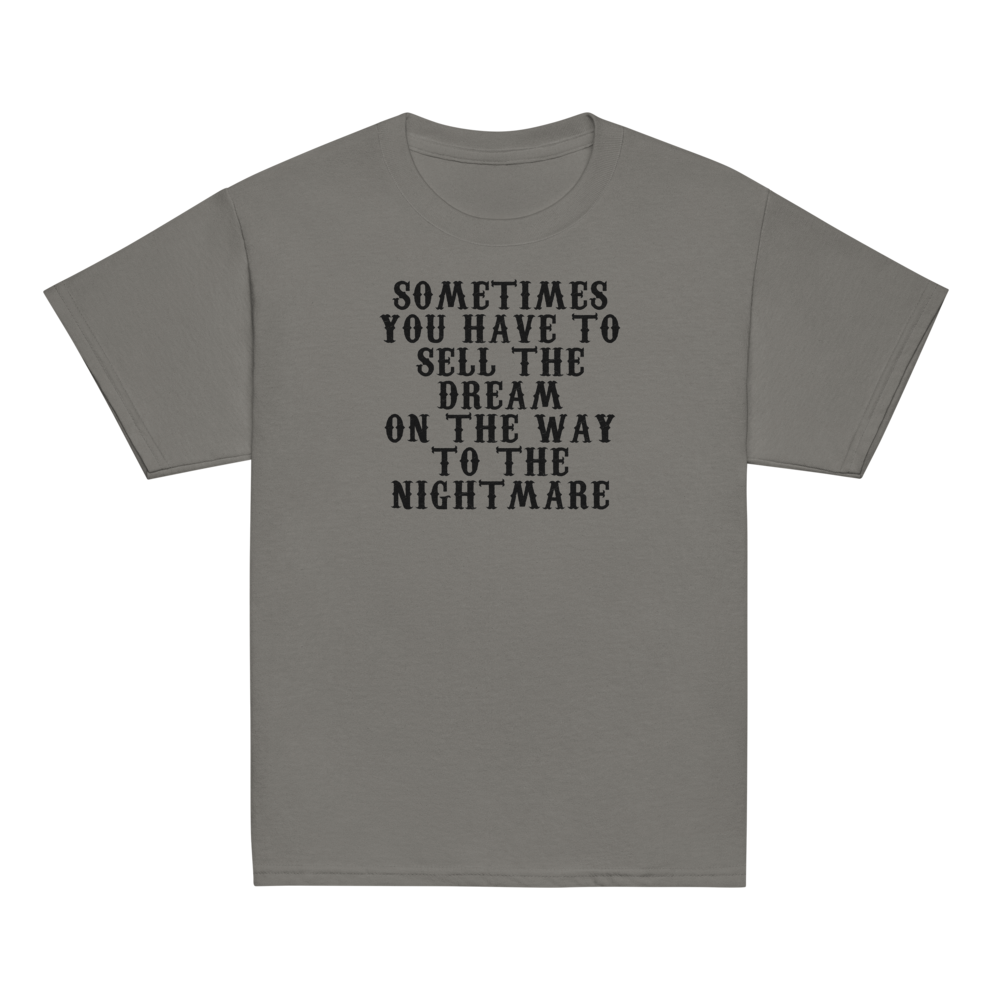"Sometimes you have to sell the dream on the way to the nightmare" printed on a charcoal youth classic tee laying on a flat surface