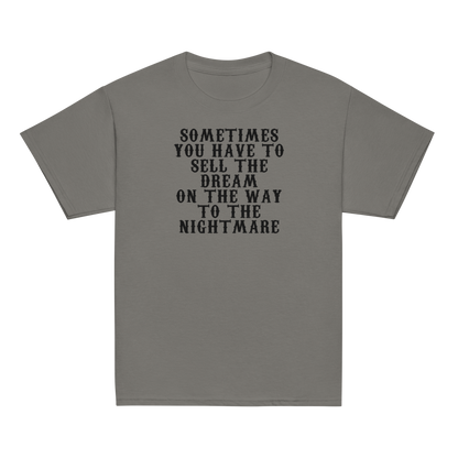 "Sometimes you have to sell the dream on the way to the nightmare" printed on a charcoal youth classic tee laying on a flat surface