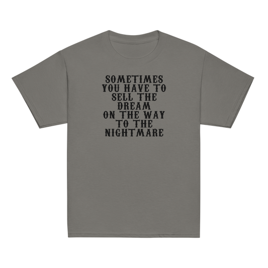 "Sometimes you have to sell the dream on the way to the nightmare" printed on a charcoal youth classic tee laying on a flat surface