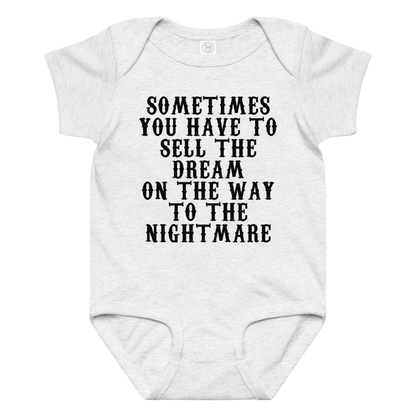 "Sometimes you have to sell the dream on the way to the nightmare" printed on a ash baby jersey bodysuit laying on a flat surface amongst other clothes
