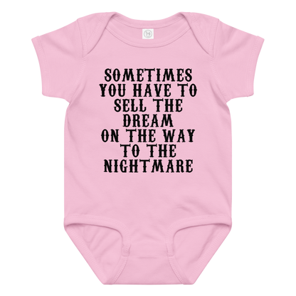 "Sometimes you have to sell the dream on the way to the nightmare" printed on a pink baby jersey bodysuit laying on a flat surface amongst other clothes