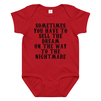 "Sometimes you have to sell the dream on the way to the nightmare" printed on a red baby jersey bodysuit laying on a flat surface amongst other clothes