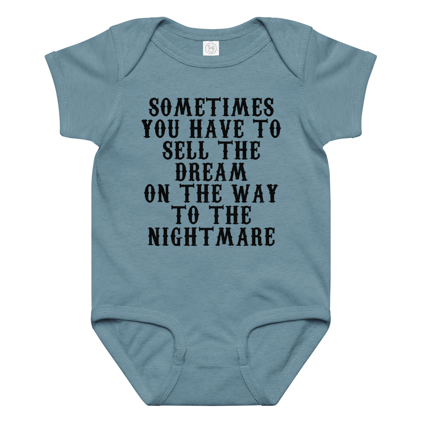 "Sometimes you have to sell the dream on the way to the nightmare" printed on a vintage indigo baby jersey bodysuit laying on a flat surface amongst other clothes