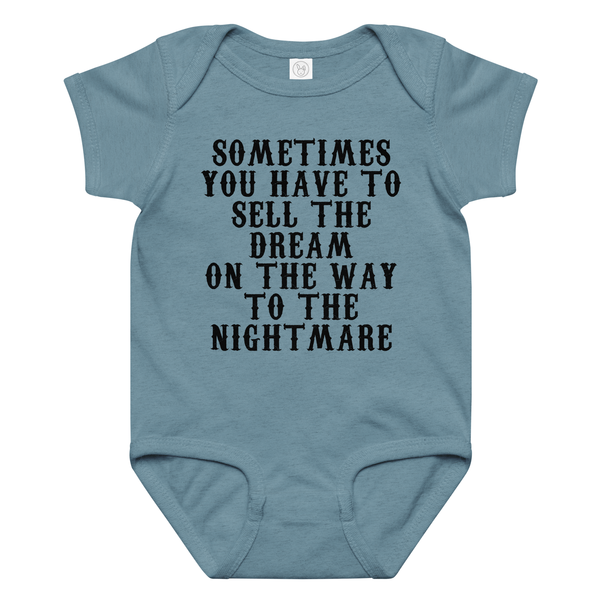 "Sometimes you have to sell the dream on the way to the nightmare" printed on a vintage indigo baby jersey bodysuit laying on a flat surface amongst other clothes