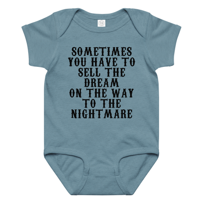 "Sometimes you have to sell the dream on the way to the nightmare" printed on a vintage indigo baby jersey bodysuit laying on a flat surface amongst other clothes