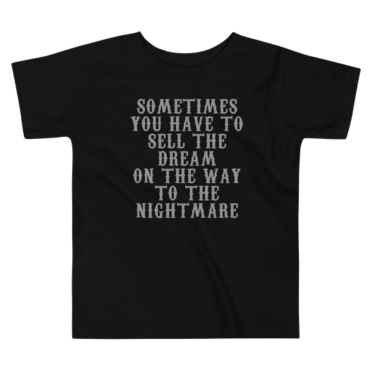 "Sometimes you have to sell the dream on the way to the nightmare" printed on a black toddler short sleeve tee laying on a flat surface