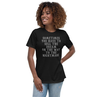 "Sometimes you have to sell the dream on the way to the nightmare" printed on a black women's relaxed t-shirt worn by a female