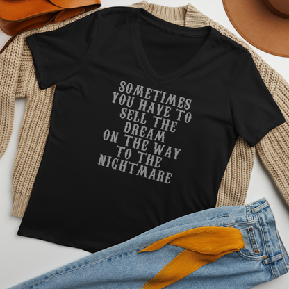 "Sometimes you have to sell the dream on the way to the nightmare" printed on a solid black blend women's relaxed v-neck t-shirt laying on a flat surface amongst other clothes