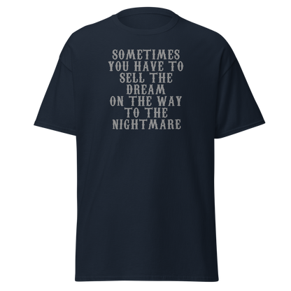 "Sometimes you have to sell the dream on the way to the nightmare" printed on a navy unisex classic tee laying on a flat surface