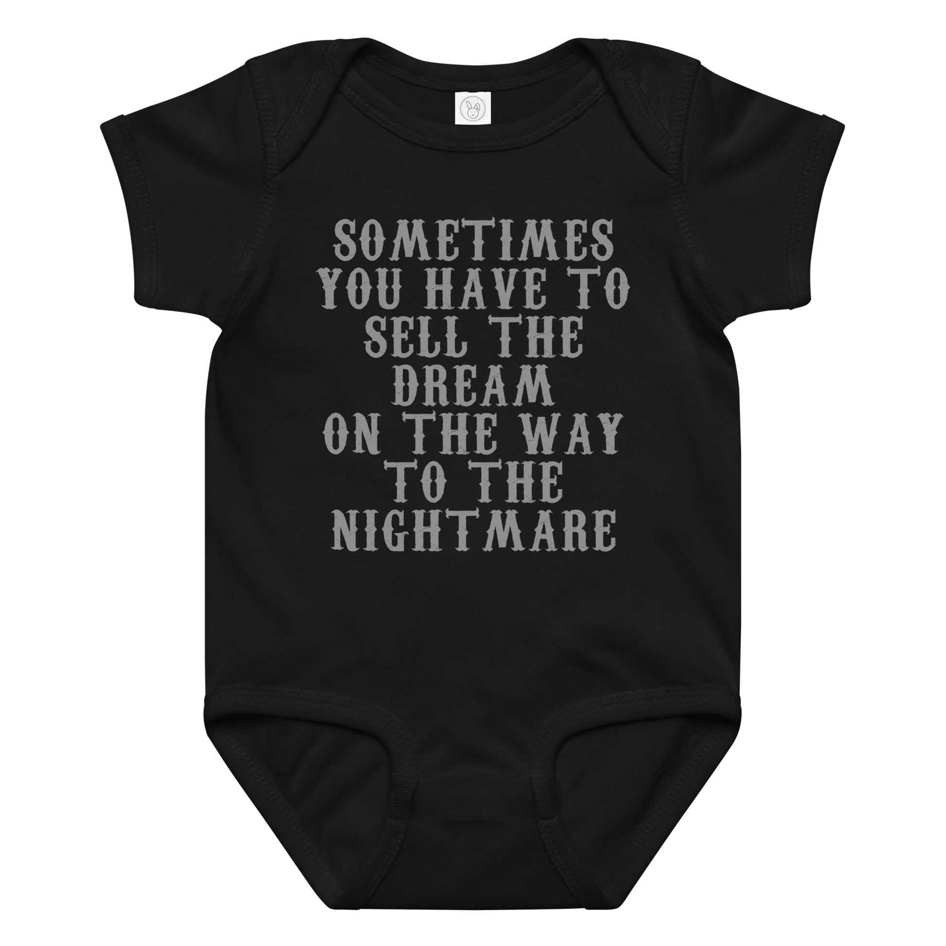 "Sometimes you have to sell the dream on the way to the nightmare" printed on a black baby jersey bodysuit laying on a flat surface amongst other clothes