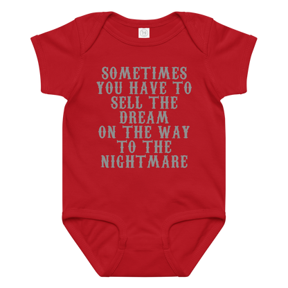 "Sometimes you have to sell the dream on the way to the nightmare" printed on a red baby jersey bodysuit laying on a flat surface amongst other clothes