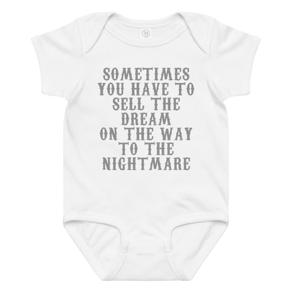 "Sometimes you have to sell the dream on the way to the nightmare" printed on a white baby jersey bodysuit laying on a flat surface amongst other clothes