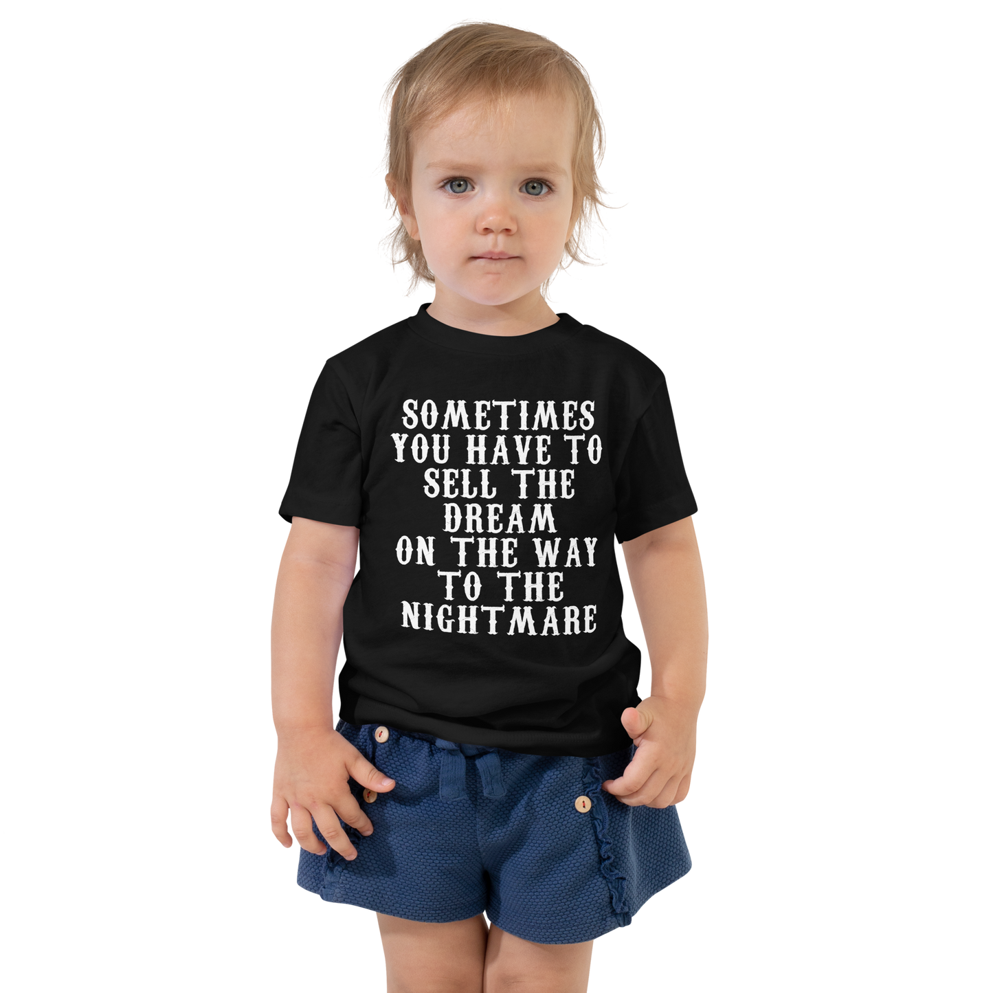 "Sometimes you have to sell the dream on the way to the nightmare" printed on a black toddler short sleeve tee worn by a female