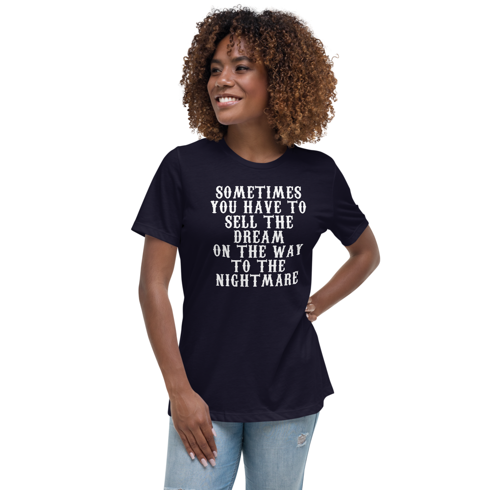 "Sometimes you have to sell the dream on the way to the nightmare" printed on a navy women's relaxed t-shirt worn by a female
