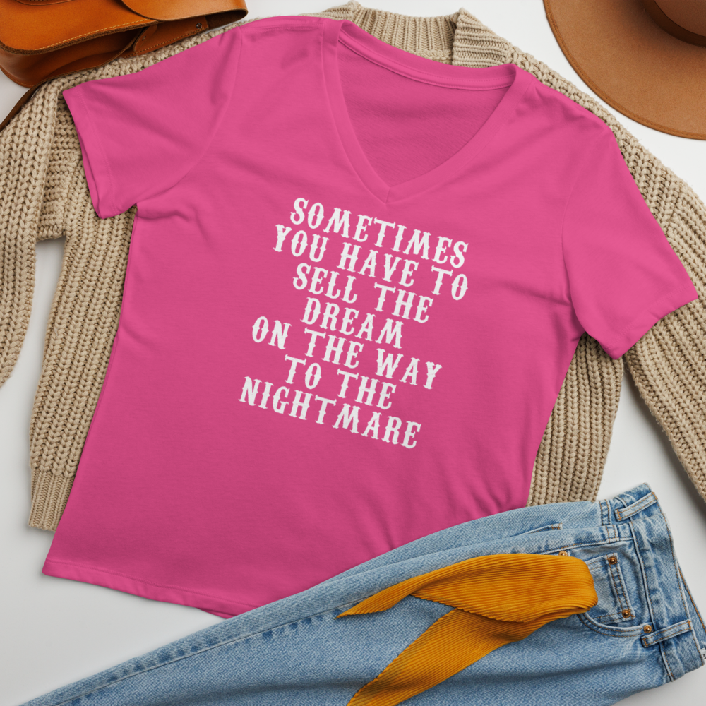 "Sometimes you have to sell the dream on the way to the nightmare" printed on a berry women's relaxed v-neck t-shirt laying on a flat surface amongst other clothes