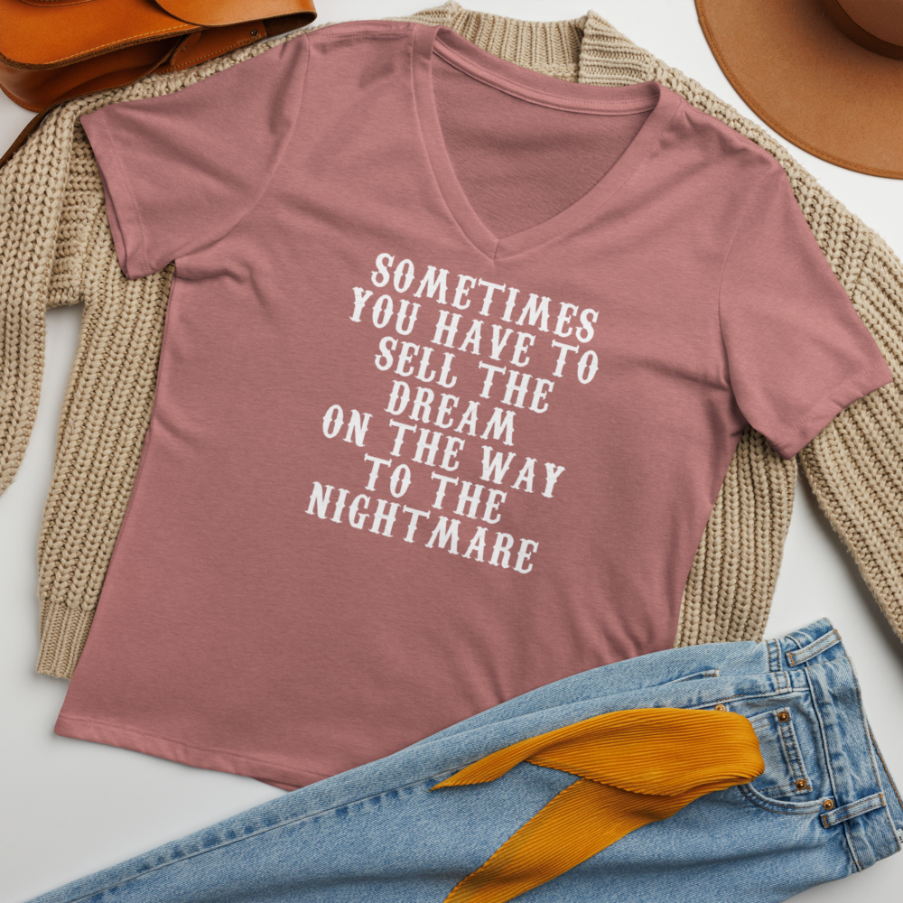 "Sometimes you have to sell the dream on the way to the nightmare" printed on a heather mauve women's relaxed v-neck t-shirt laying on a flat surface amongst other clothes